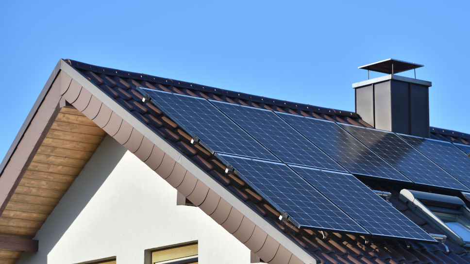 Solar panels installed on the roof of a house with tiles in Europe against the background of a blue sky.